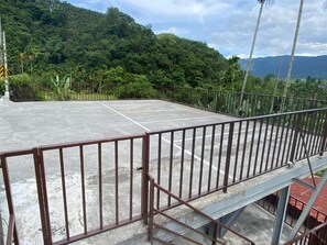 A concrete outdoor area with a metal railing, surrounded by lush greenery and hills in the background. - Atayal Villa (Datong)