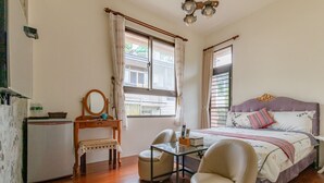 A bedroom with a bed, a desk, a chair, a small table, and a window with curtains. - Atayal Villa (Datong)