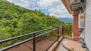 A balcony with a glass railing overlooking a lush green forest and mountains. - Atayal Villa (Datong)