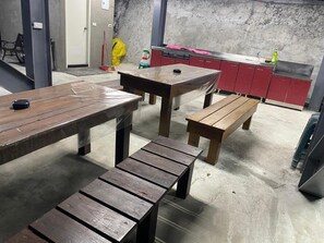 A room with a concrete floor, a wooden bench, a table, and a kitchenette area with red cabinets and a stainless steel sink. - Atayal Villa (Datong)