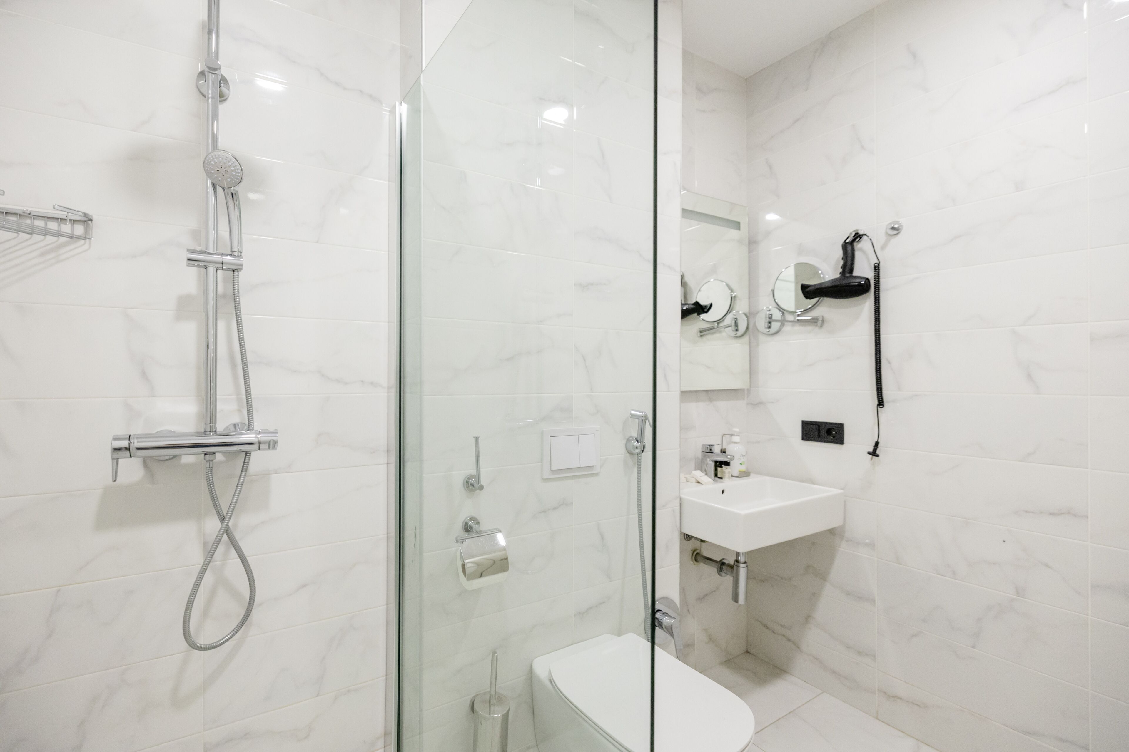 Un bany modern amb dutxa de vidre, un lavabo blanc i un mirall.