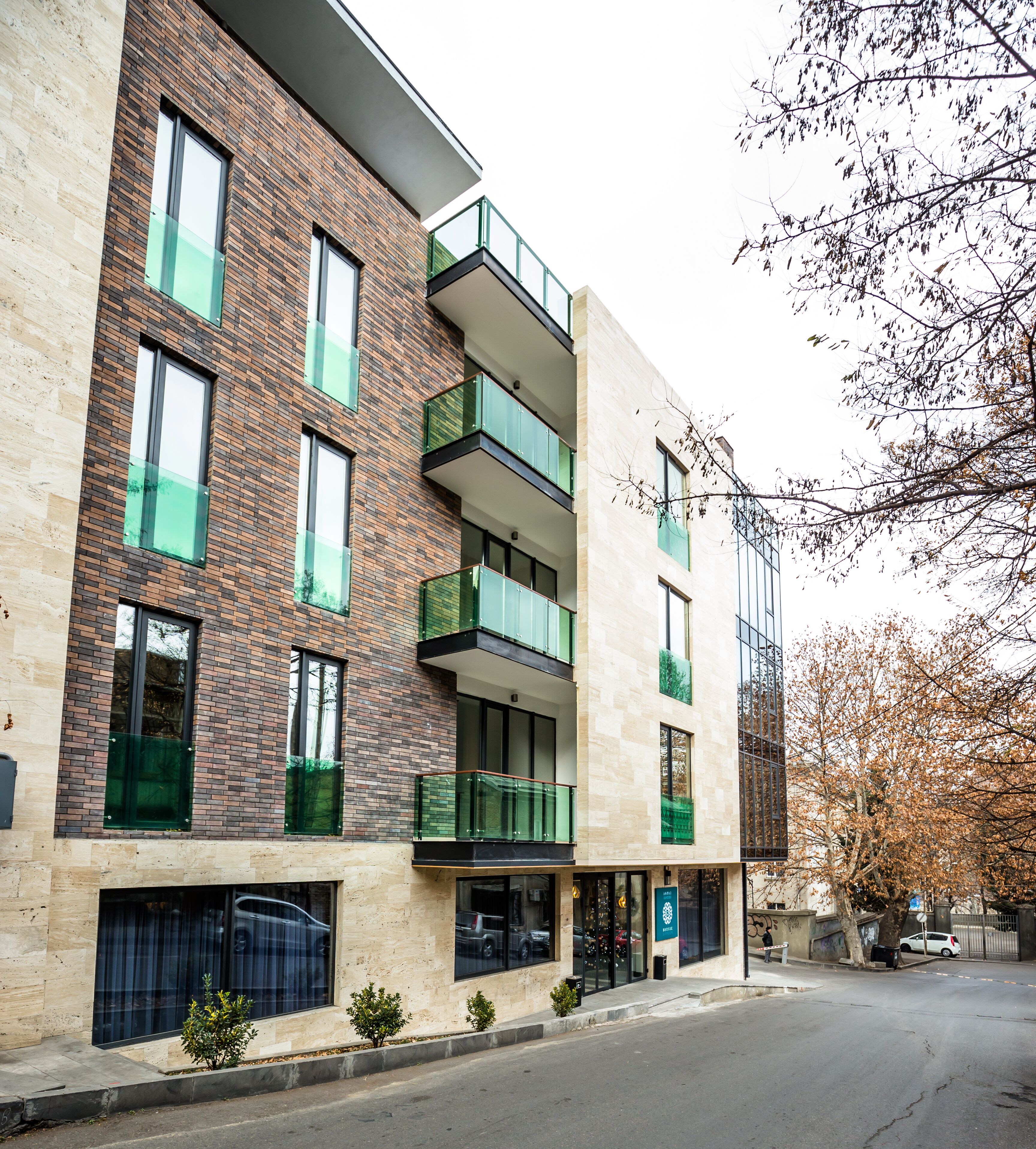 A multi-story building with a brick facade, large windows, and balconies with glass railings.