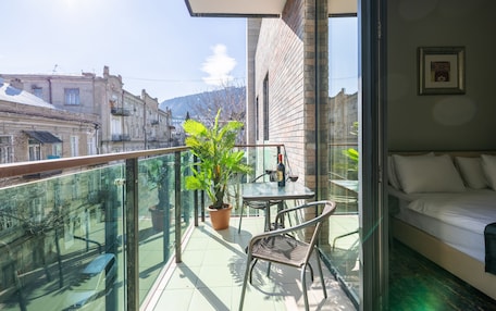 A balcony with a glass railing, a potted plant, a table with a bottle and glasses, and a sofa.