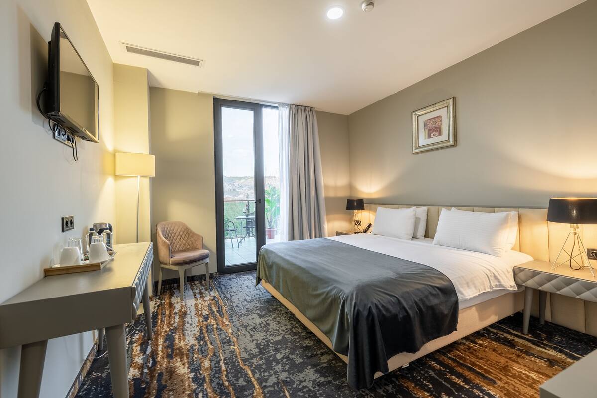 A hotel room with a bed, desk, chair, and a view of the outdoors.