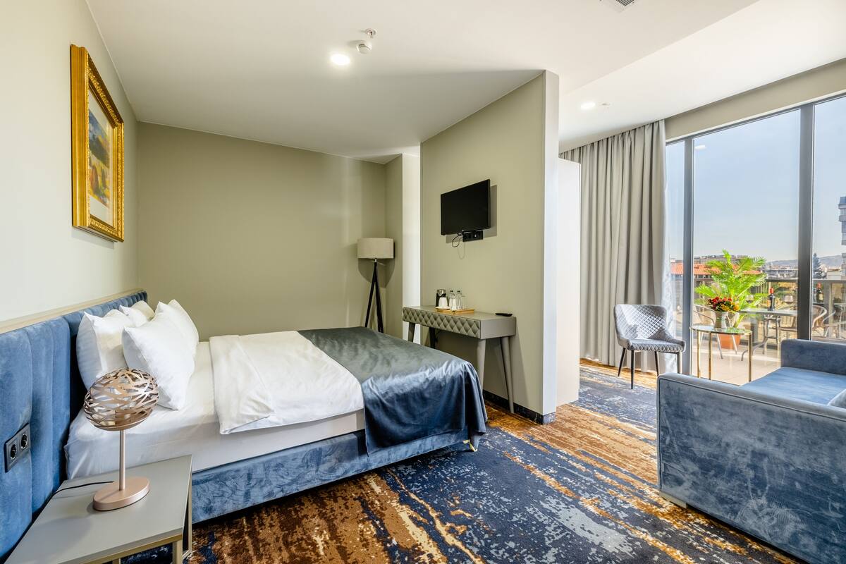 A hotel room with a bed, a desk, a TV, a chair, and a balcony with a view.