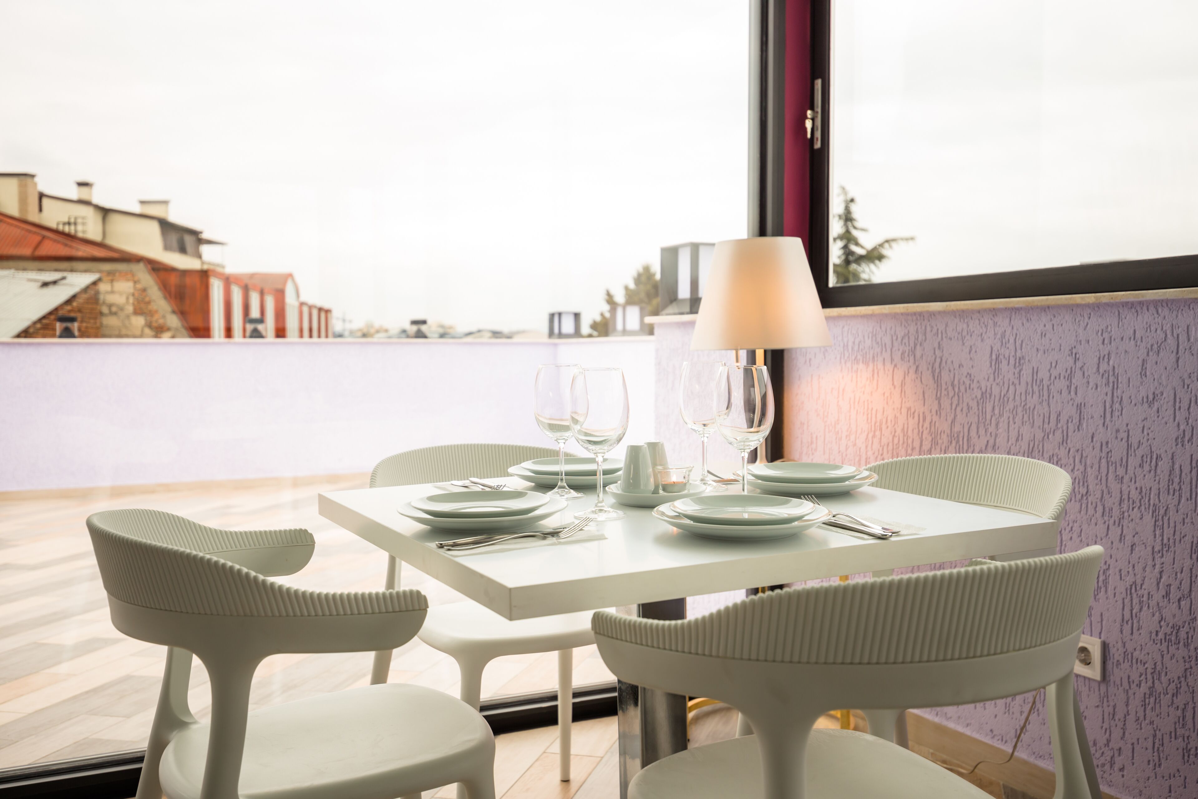 Un coin repas avec une table blanche dressée pour quatre personnes, comprenant des assiettes, des verres et des couverts.