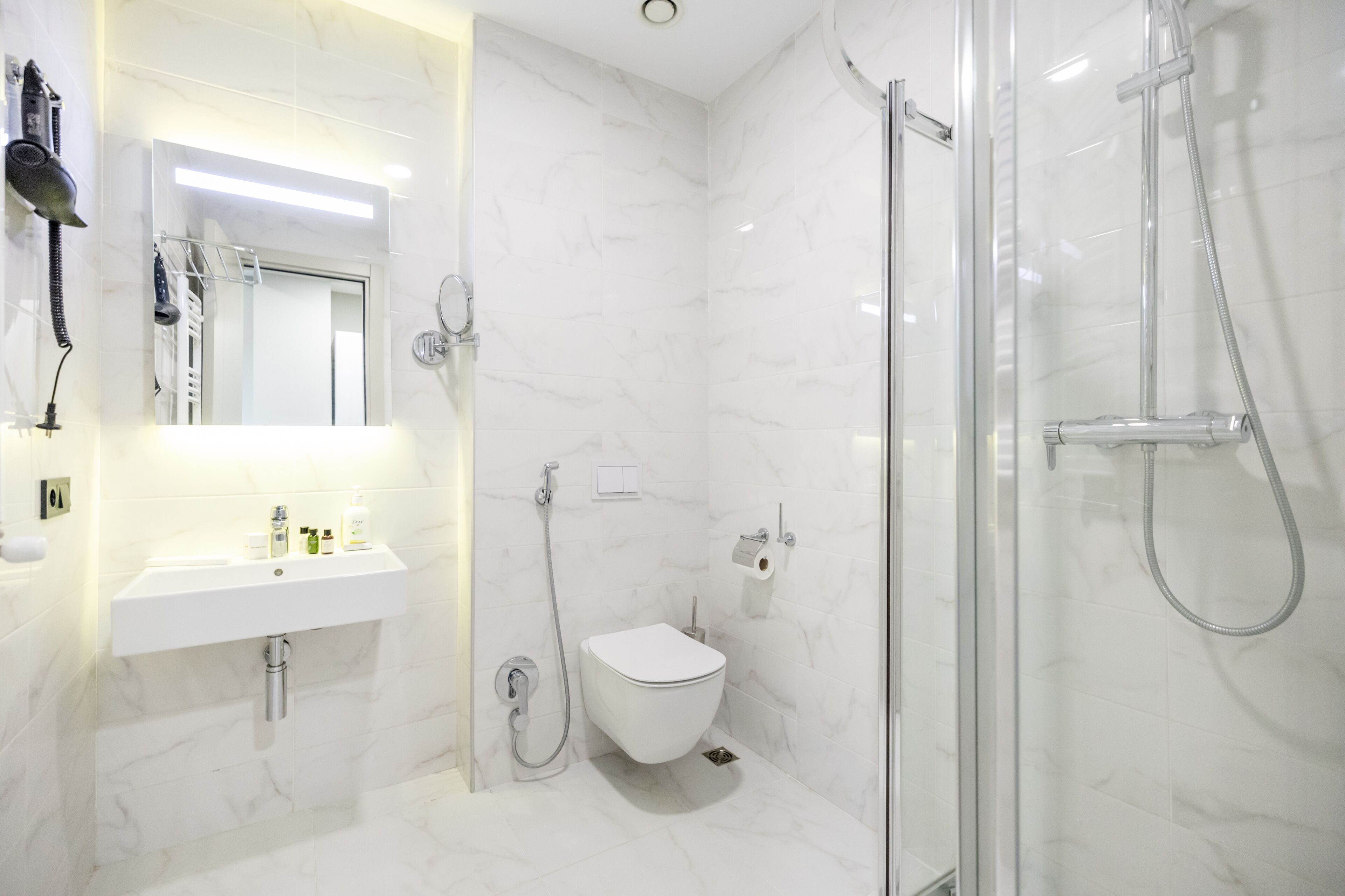 A modern bathroom with a white marble sink, a glass-enclosed shower, and a toilet.