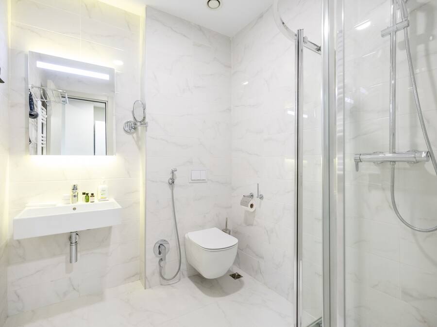 A modern bathroom with a white marble sink, a glass-enclosed shower, and a toilet.