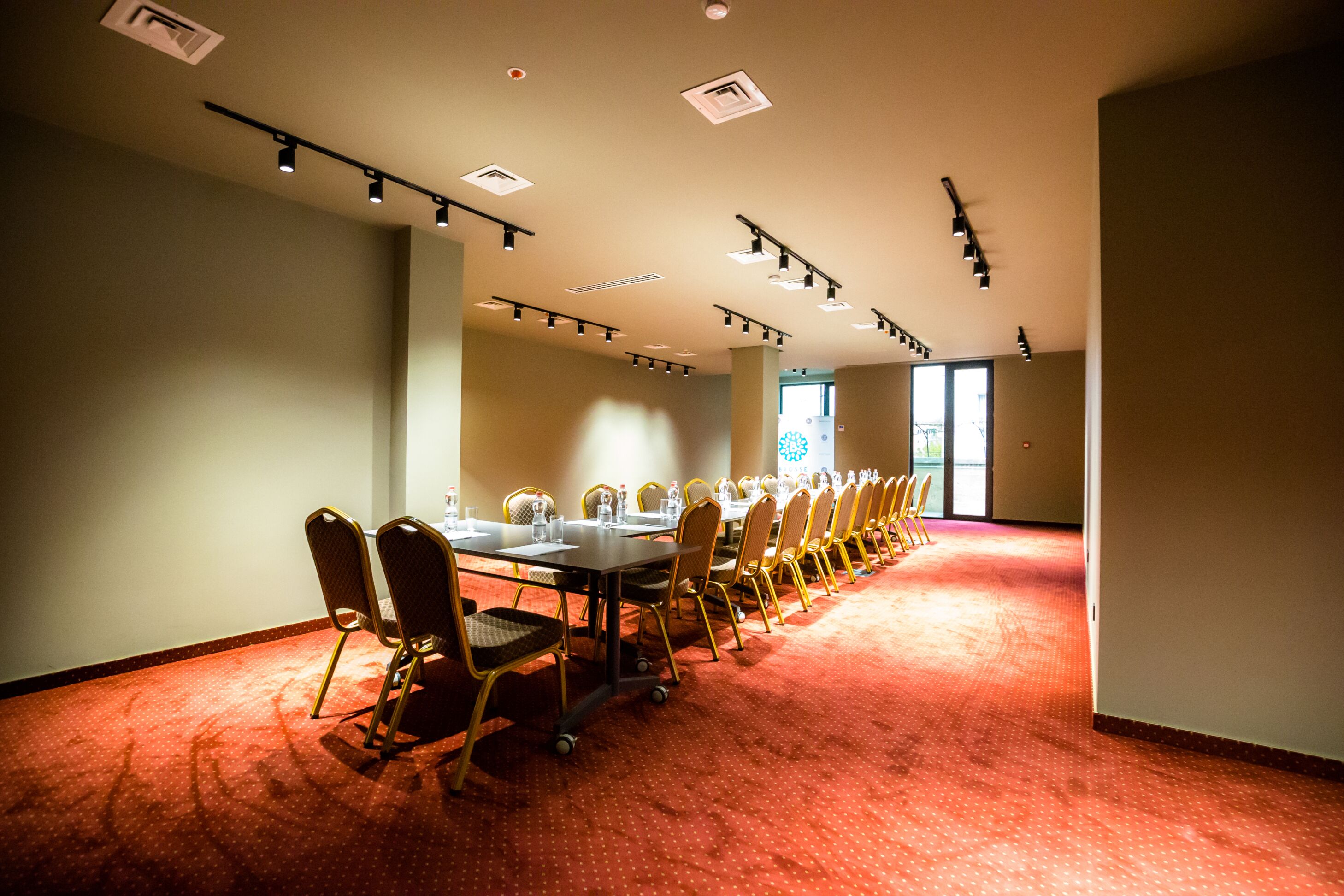 A conference room with a long table, rows of chairs, and ceiling lights.