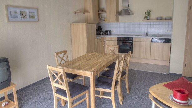A compact kitchen with wooden cabinets, a dining table with chairs, a small television, and a red object on a side table. - Quiet and yet centrally located in Binz (Binz)