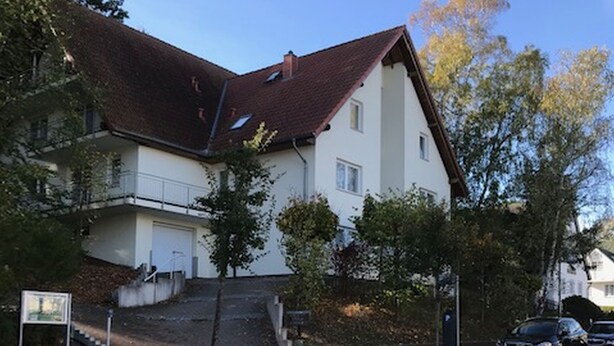A residential building with a steeply pitched roof, a visible staircase leading to a second-floor balcony, and a red bike lane on the street.