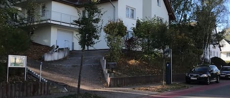 A residential building with a steeply pitched roof, a visible staircase leading to a second-floor balcony, and a red bike lane on the street.