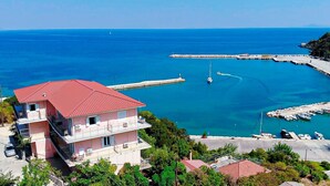 A coastal building with balconies overlooking a marina with boats and a pier. - Faro Del Porto (Kefalonia)