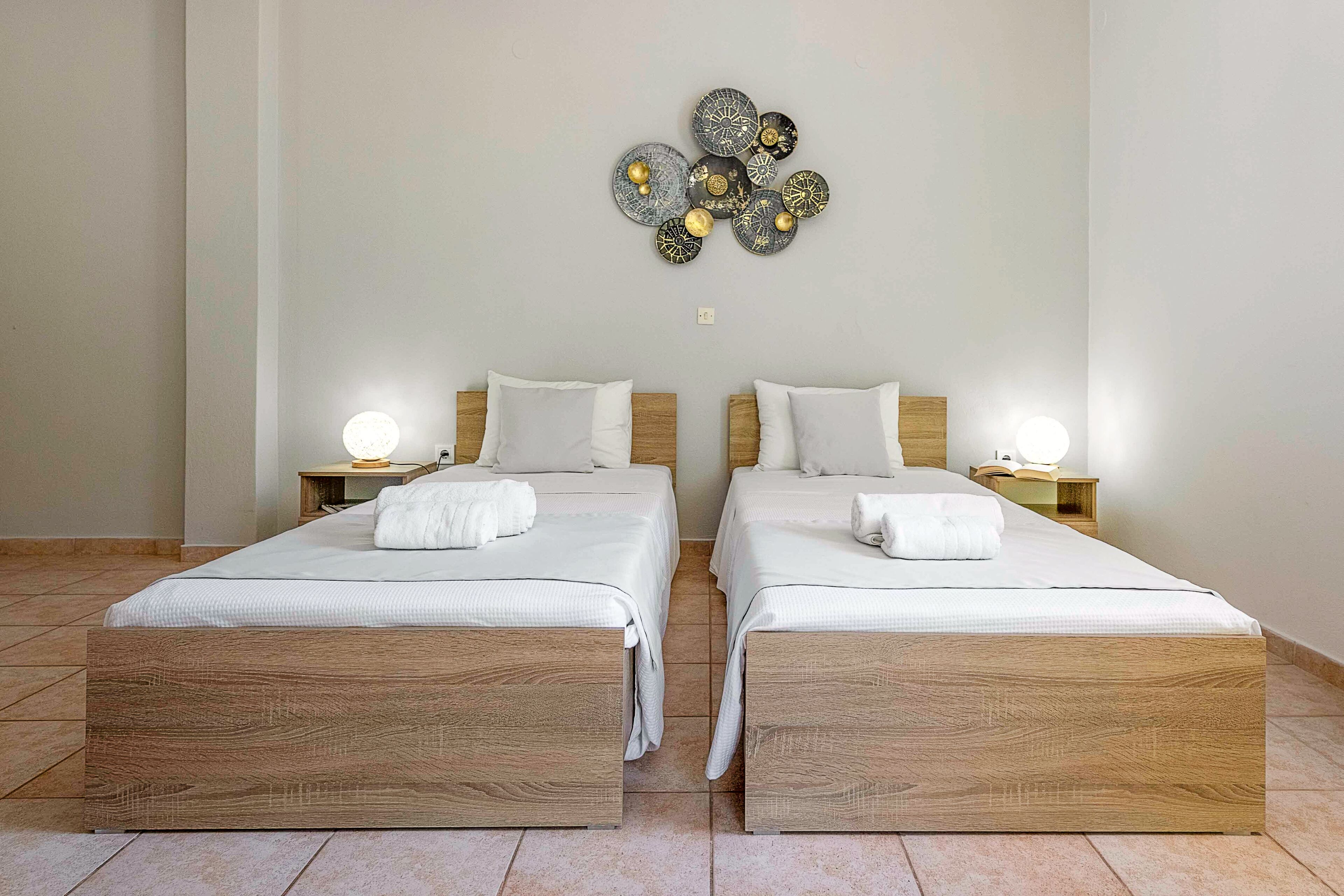 Une chambre double avec deux lits, chacun doté d’une tête de lit en bois, de linge de lit blanc et d’une lampe de chevet.