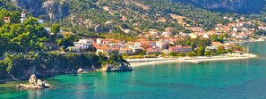 A coastal town with buildings along the shoreline, a lighthouse, and rocky outcrops. - Faro Del Porto (Kefalonia)