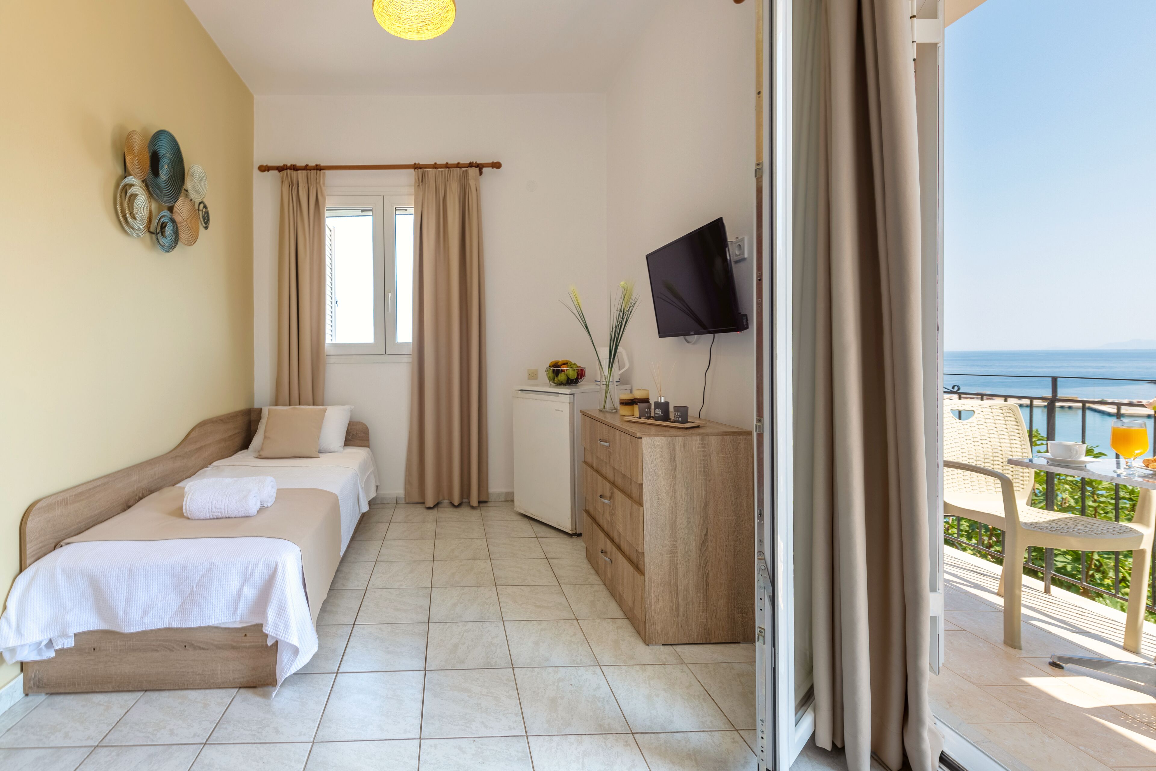 Habitación de hotel con dos camas, televisión, un escritorio pequeño y un balcón con mesa y sillas.