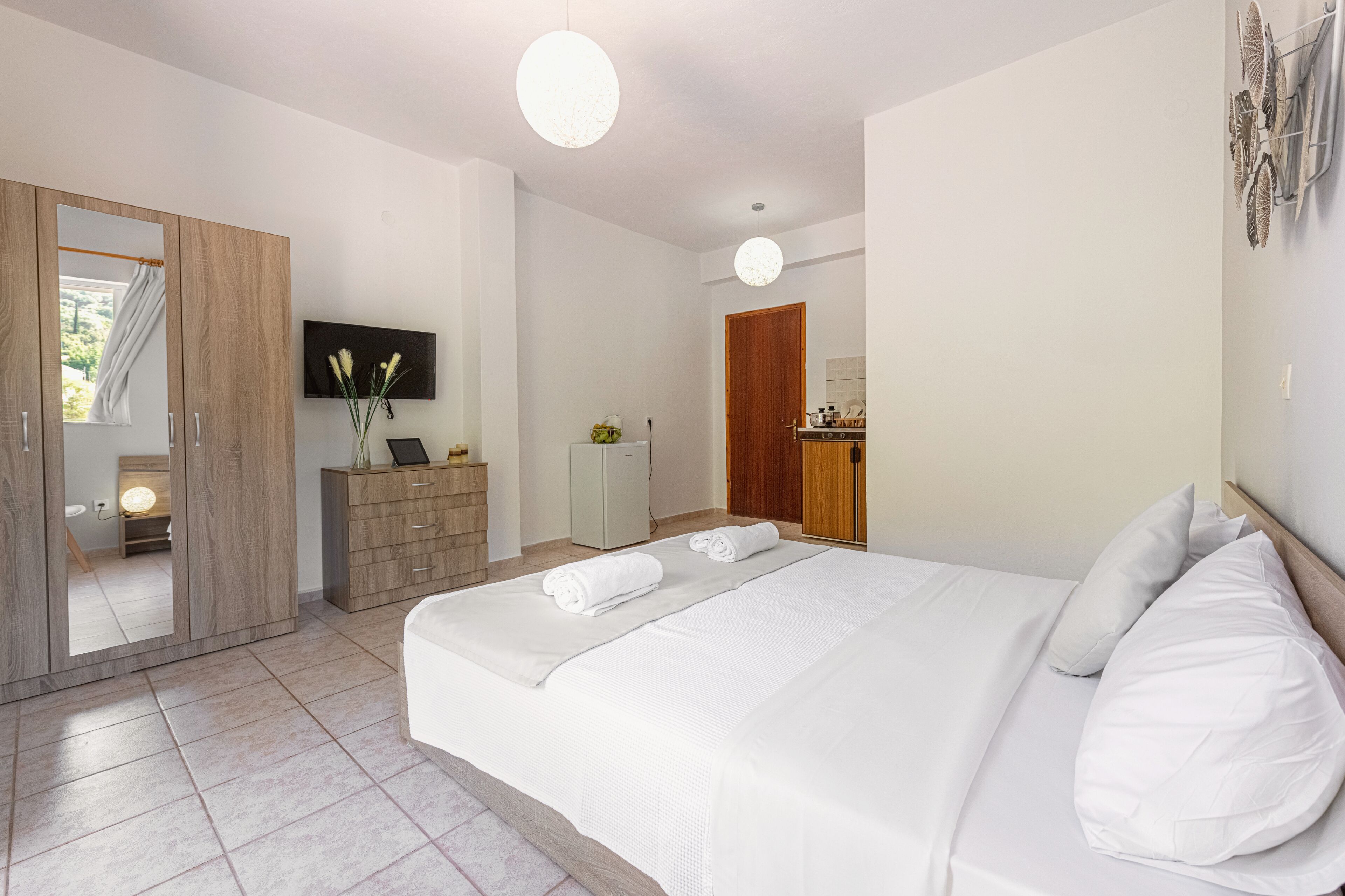Una habitación de hotel moderna con una cama grande, un armario, un televisor y una pequeña kitchenette.