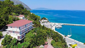 A coastal building with a red roof, surrounded by lush greenery and a marina with boats. - Faro Del Porto (Kefalonia)