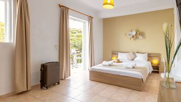 A hotel room with a large bed, a suitcase, a balcony, and a view of greenery outside.