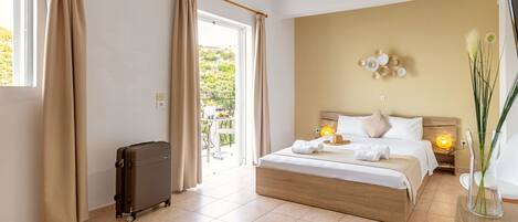 A hotel room with a large bed, a suitcase, a balcony, and a view of greenery outside.