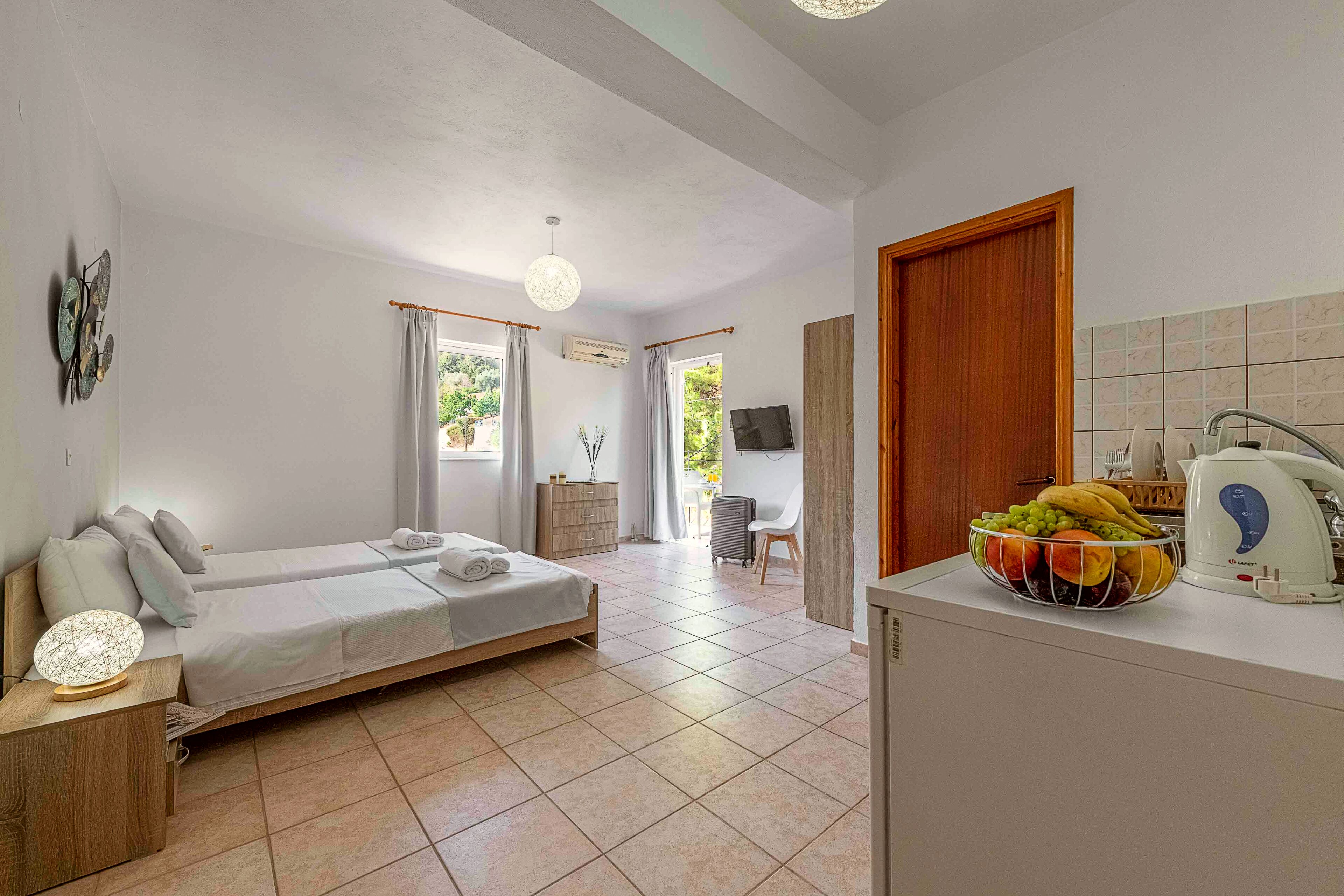 Een kamer met een bed, een bureau, een keukenhoek met een schaal fruit en uitzicht op de omgeving.