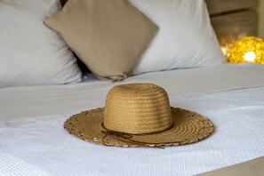 A straw hat on a bed with white bedding and a beige pillow in the background. - Faro Del Porto (Kefalonia)