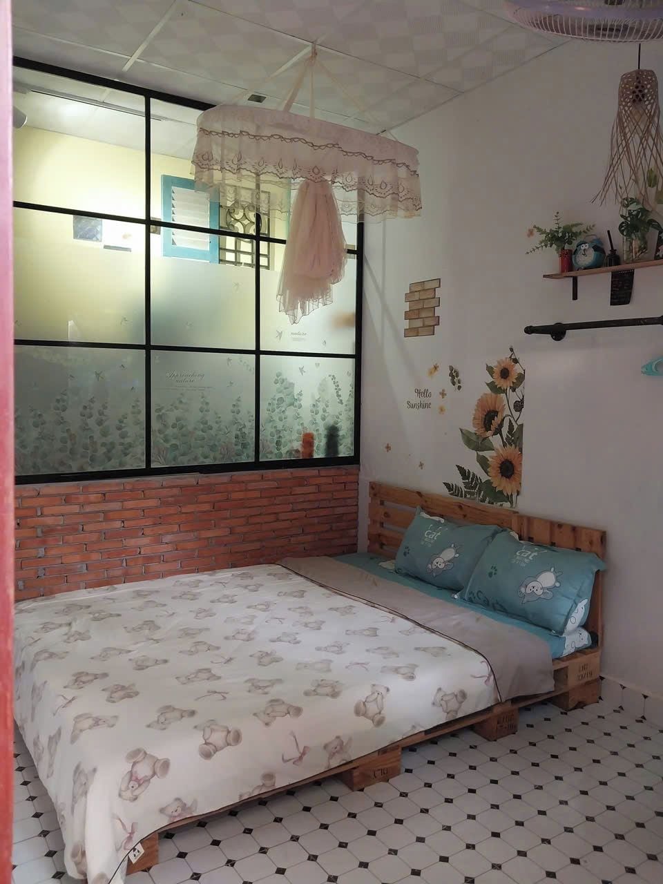 A bedroom with a bed, a window with frosted glass, a brick wall, and a wall with a sunflower mural.