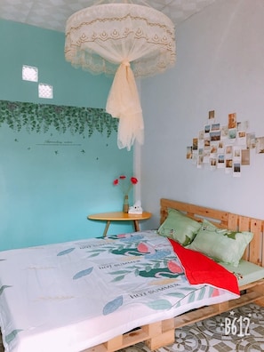 Une chambre à coucher avec un lit, une table de chevet, un mur décoré de photos et une moustiquaire suspendue.