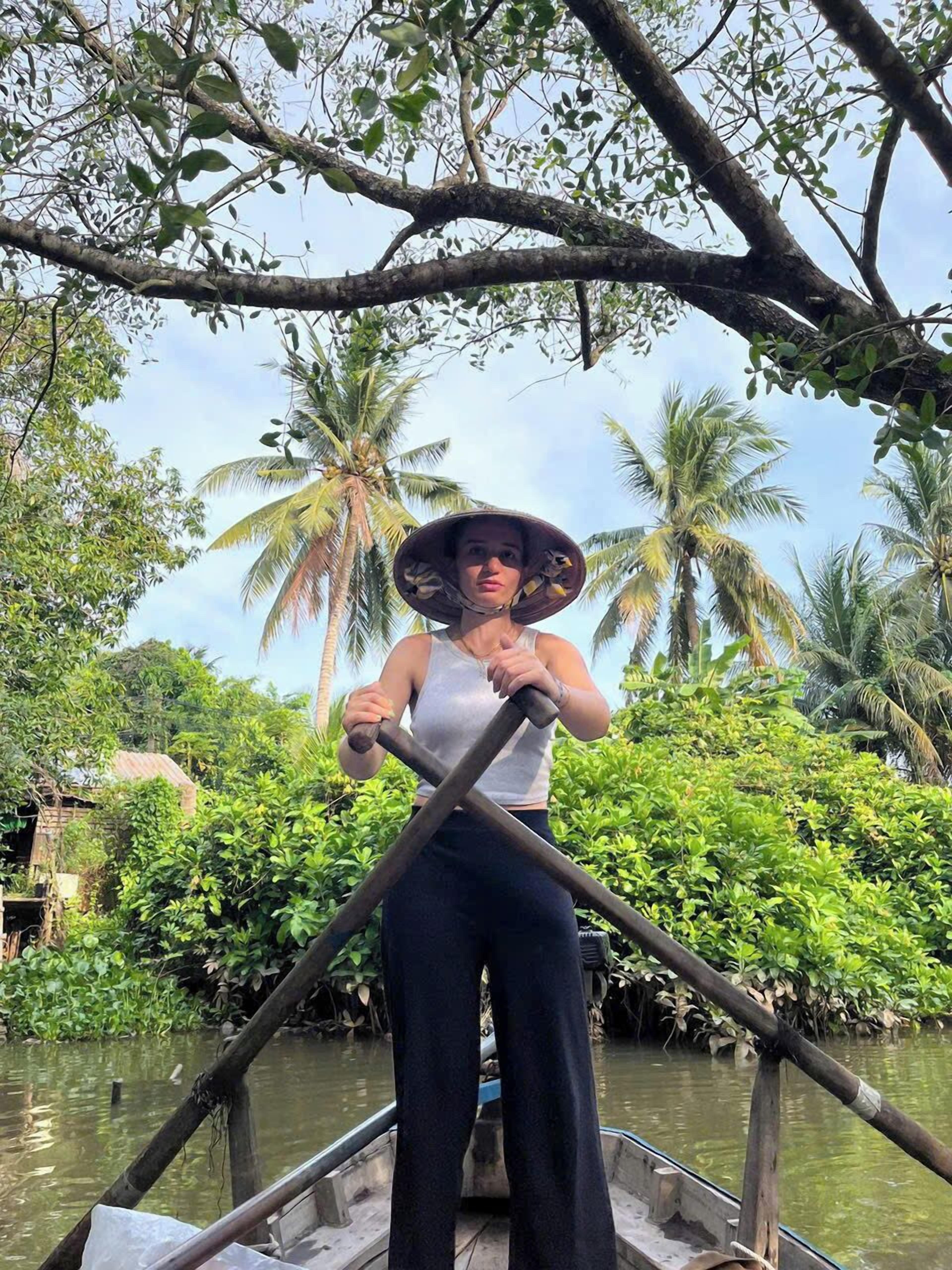 A person rowing a boat in a natural setting with palm trees and dense foliage in the background.