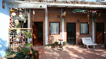 Un bâtiment en briques avec un patio carrelé, des plantes en pot, un banc blanc et des décorations suspendues.