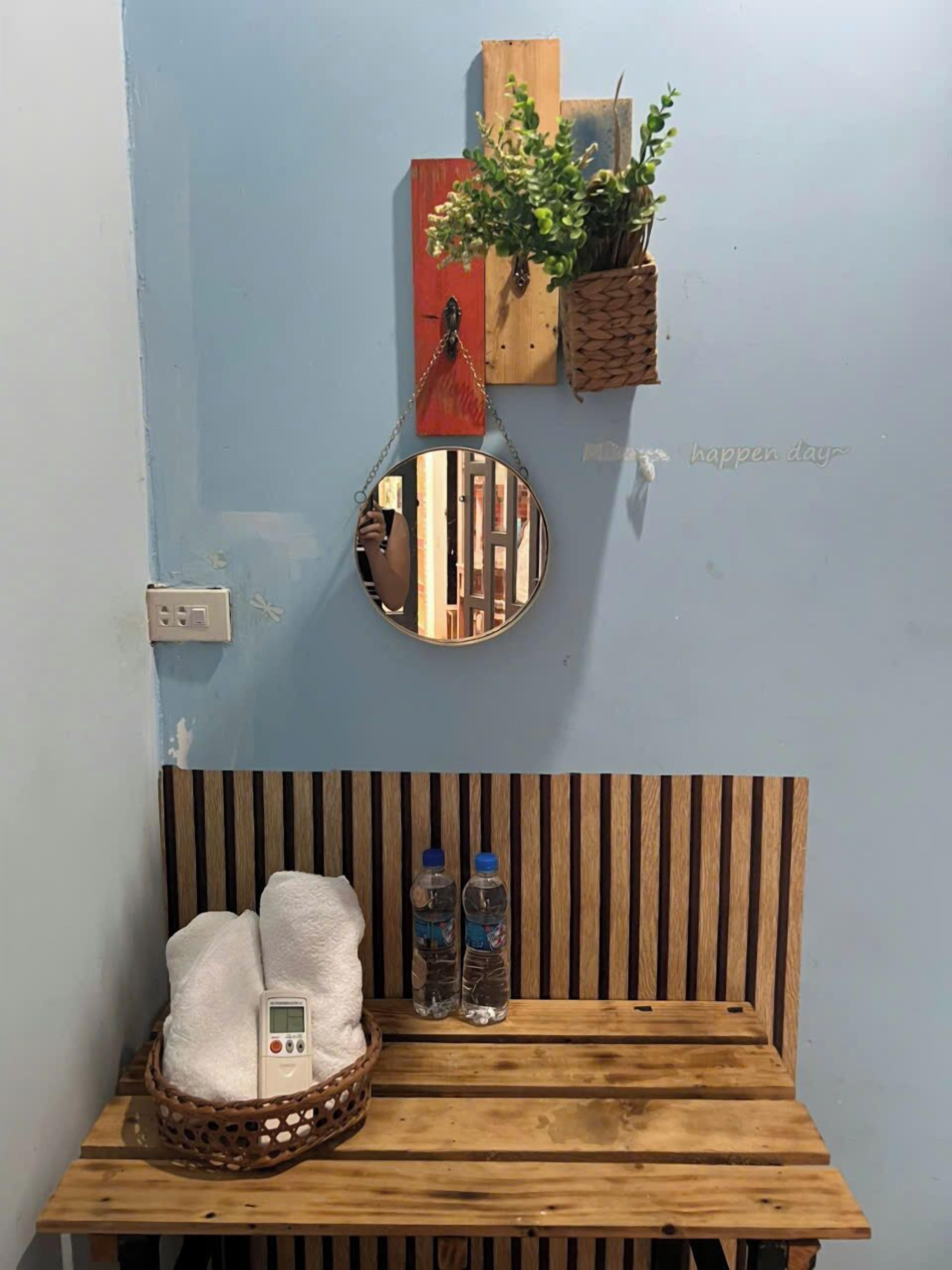 Un banco de madera con una cesta tejida que contiene toallas y un termómetro digital. Encima, paneles de madera y un espejo colgante.
