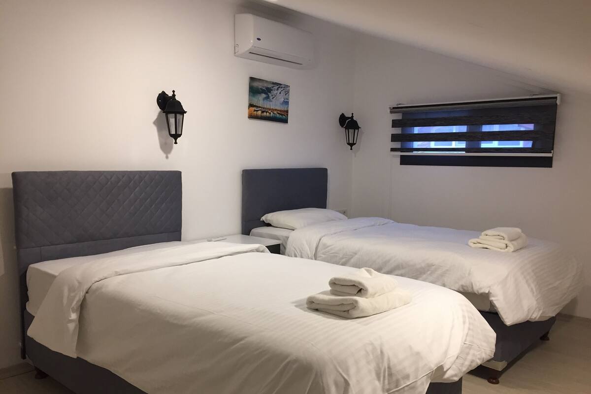 A hotel room with two beds, white linens, a painting on the wall, and a window with blinds.