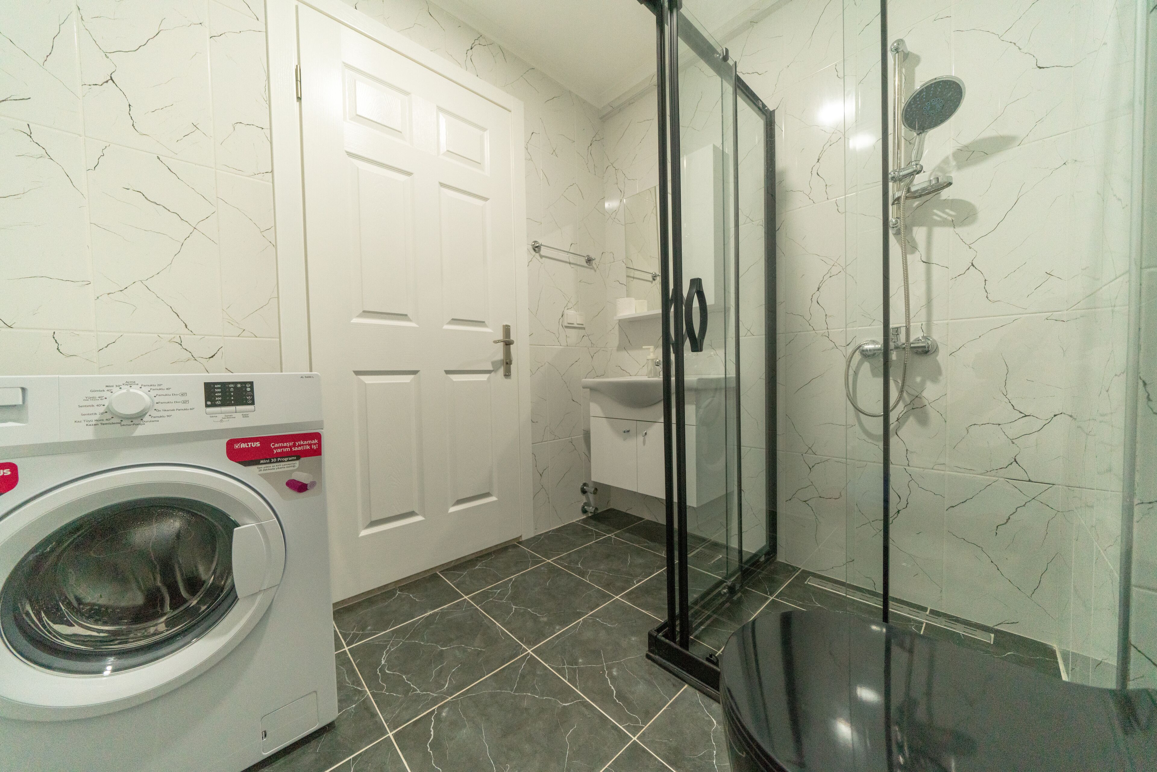 A bathroom with a washing machine, a glass shower enclosure, and a white door.