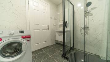 A bathroom with a washing machine, a glass shower enclosure, and a white door.