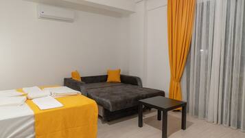A hotel room with a bed, a sofa, a small table, and a window with curtains.
