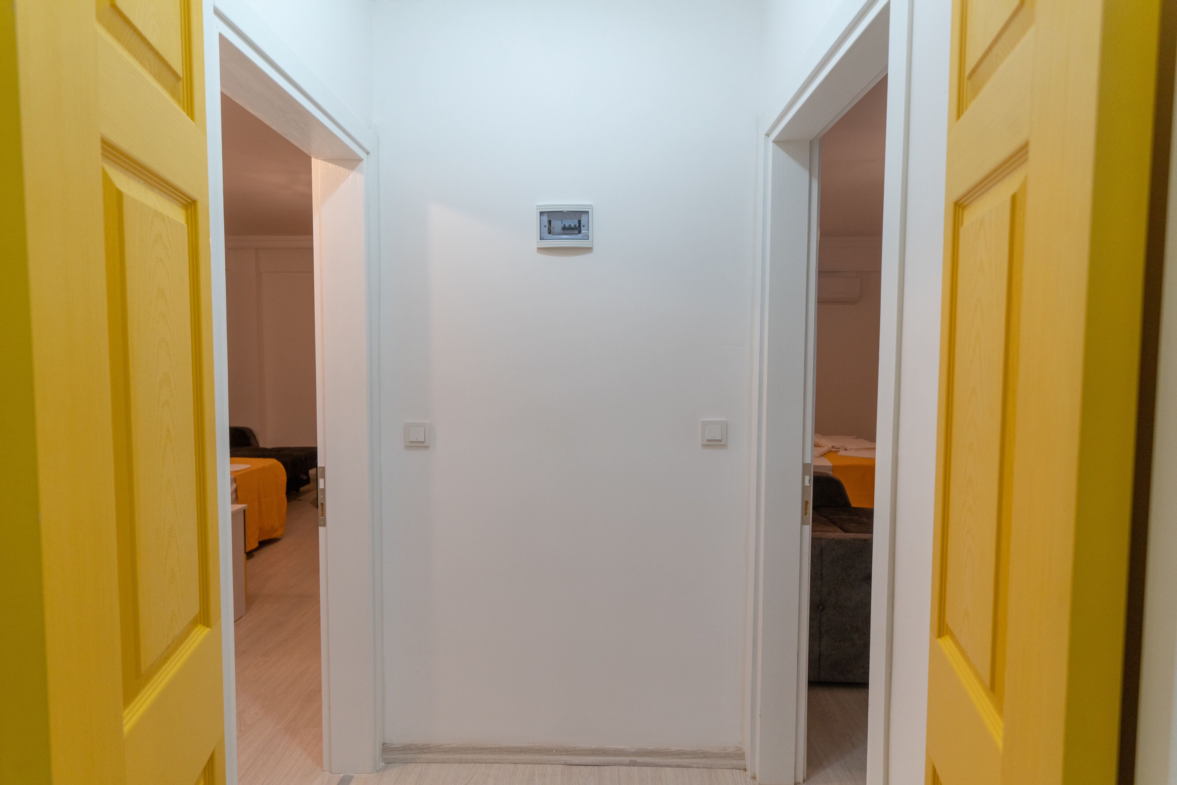 A hallway with yellow doors leading to a room with a bed and a small table.