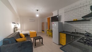 A compact living space with a sofa, a small table, a kitchen area with a refrigerator, and a dining area with a chair and table. - F48 Homes (Fethiye)