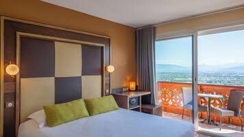Habitación de hotel con cama, escritorio y balcón con vistas.