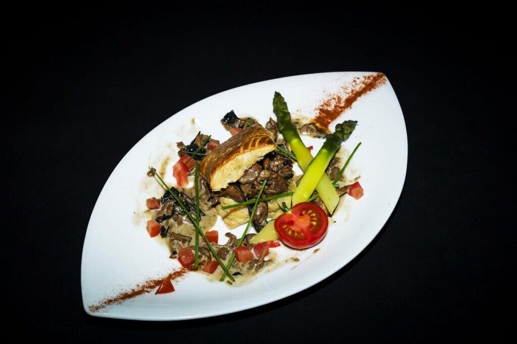 A white plate with a dish containing mushrooms, asparagus, and tomato slices.