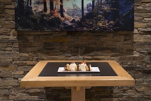 Mesa de jantar com um prato de sobremesa em frente a uma parede de pedra com uma pintura em cima.