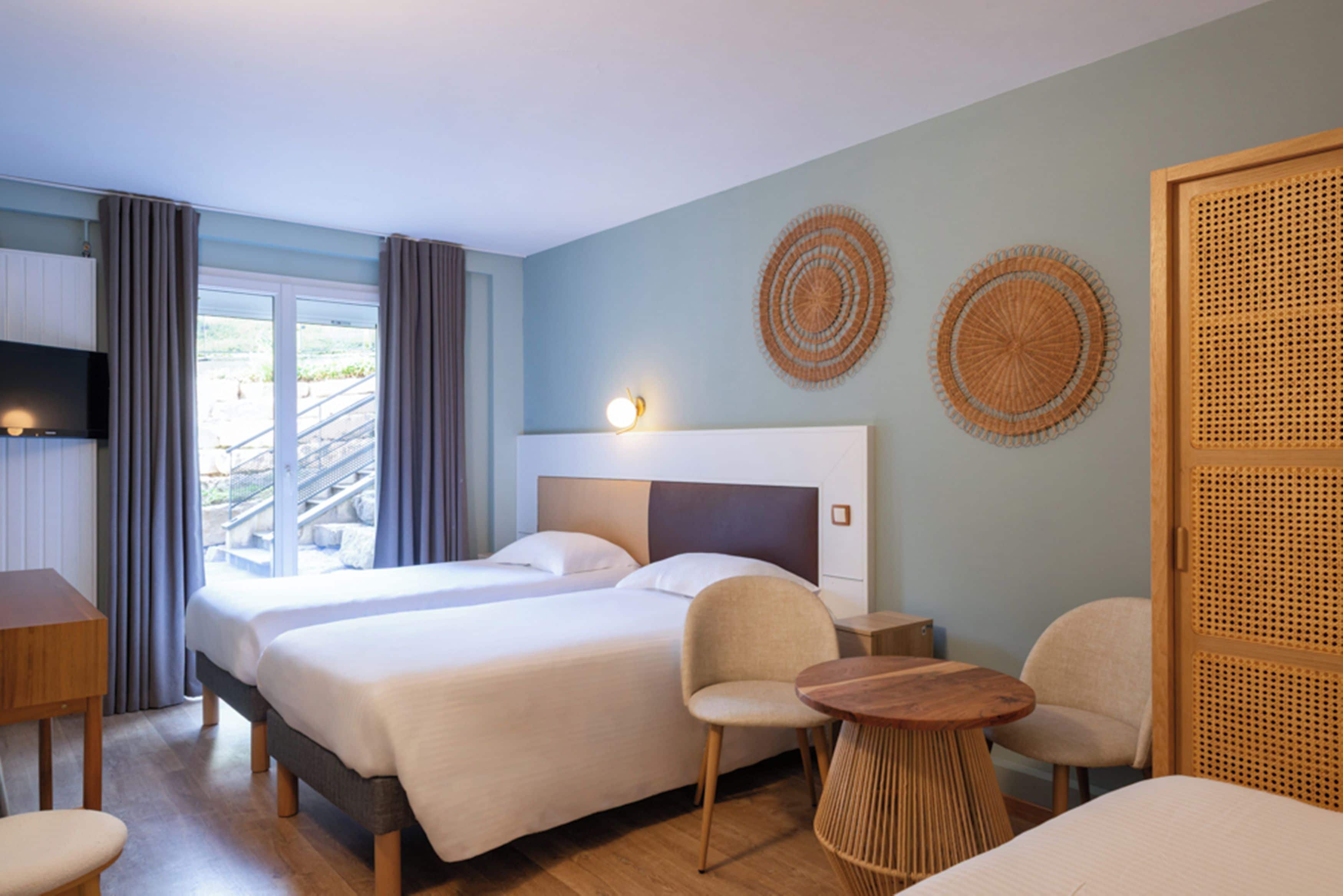 Habitación de hotel con dos camas, un televisor, una mesita y dos sillas.