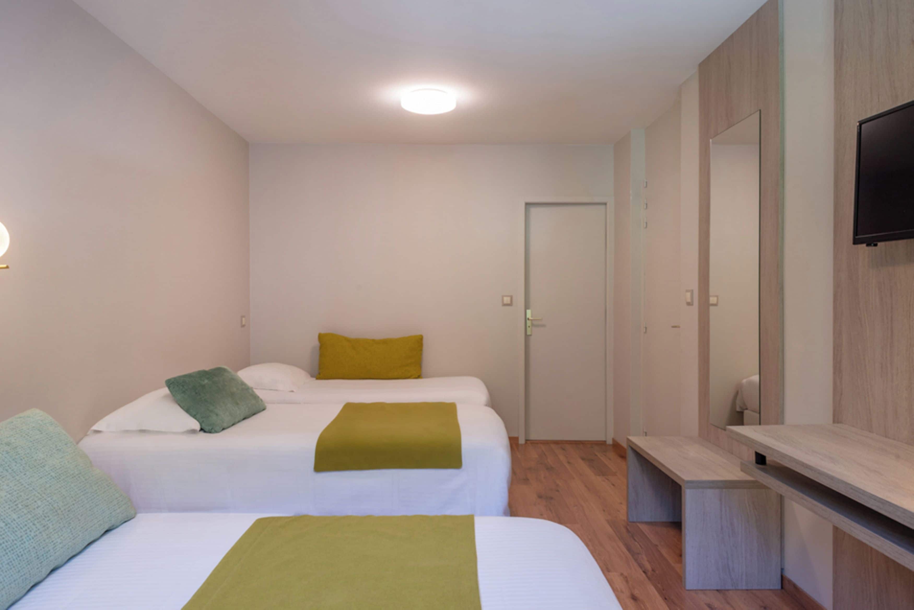 A hotel room with two beds, a TV, a wardrobe, and a desk.