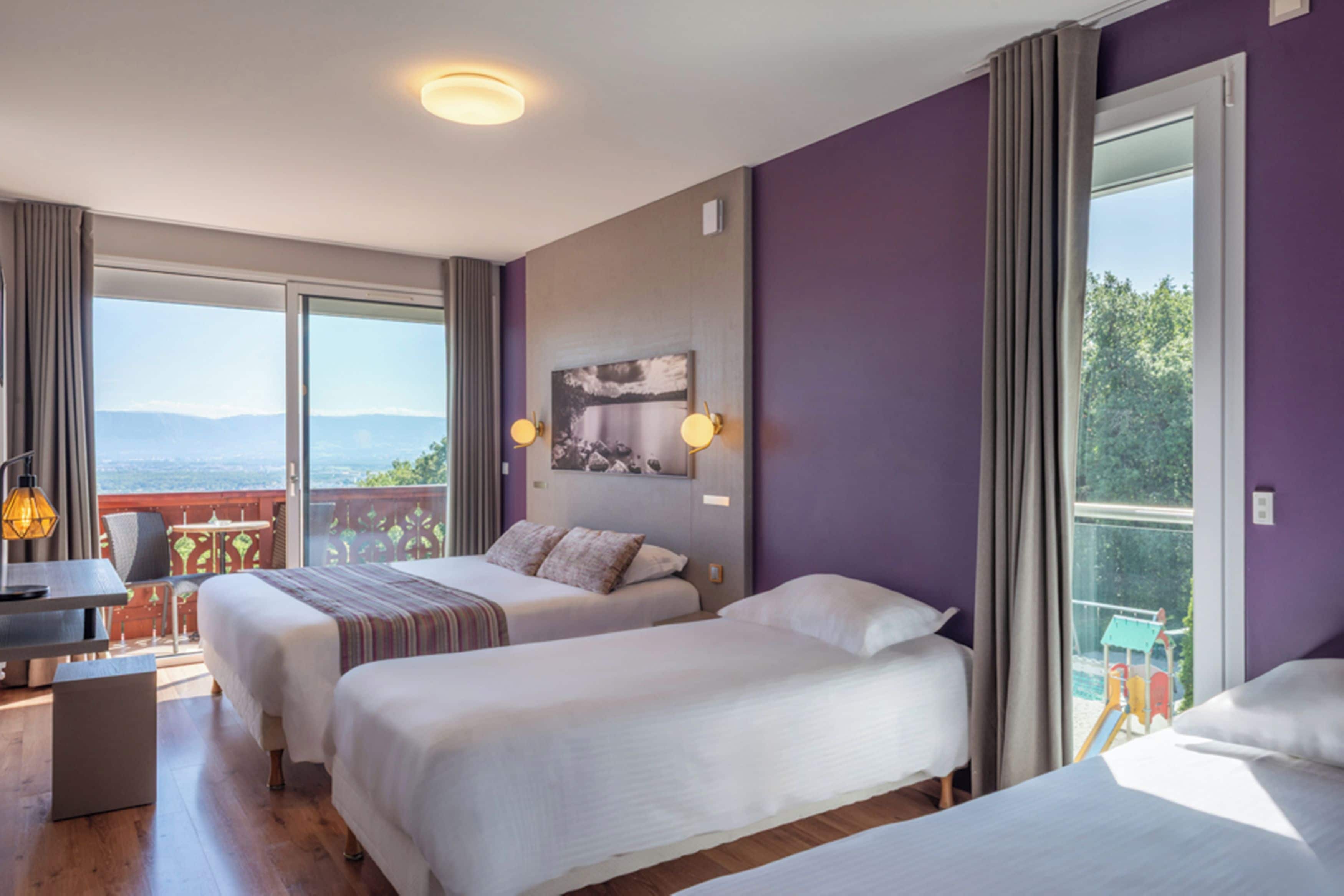 Een hotelkamer met twee bedden, een bureau en een balkon met uitzicht.