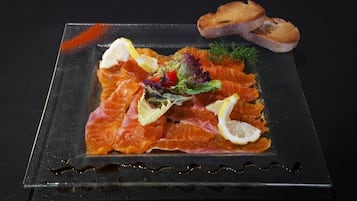 Un plato de salmón ahumado con rodajas de limón, una ensalada y pan tostado sobre una mesa oscura.