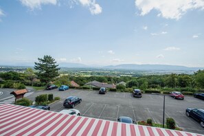 Un estacionamiento con coches y vistas a un paisaje verde con árboles y montañas distantes.