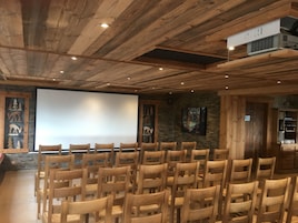 Uma sala com painéis de madeira, uma tela de projetor, cadeiras de madeira e uma parede de pedra com esculturas de animais.