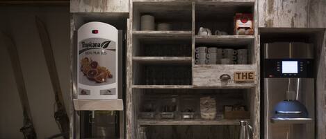 A kitchen with a refrigerator, a coffee machine, and shelves with kitchenware and jars.
