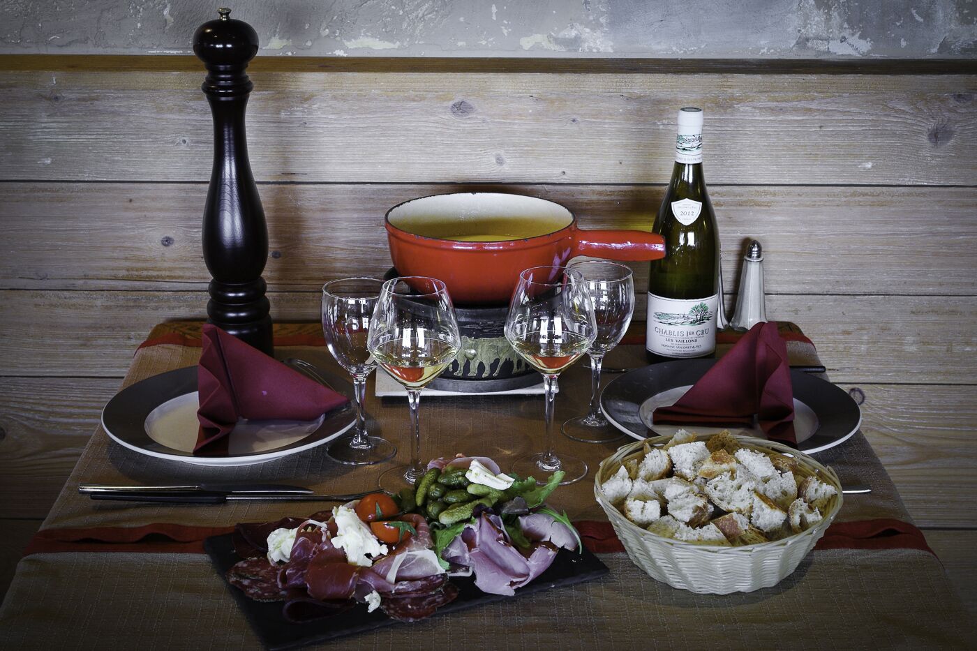 Une table mise pour un repas, avec des assiettes, des verres, une bouteille de vin, un moulin à poivre et un panier de pain.
