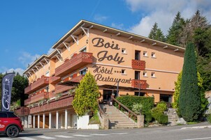Un hotel con un letrero que dice 'Bois Joly Hotel Restaurant' y un coche rojo estacionado al frente.