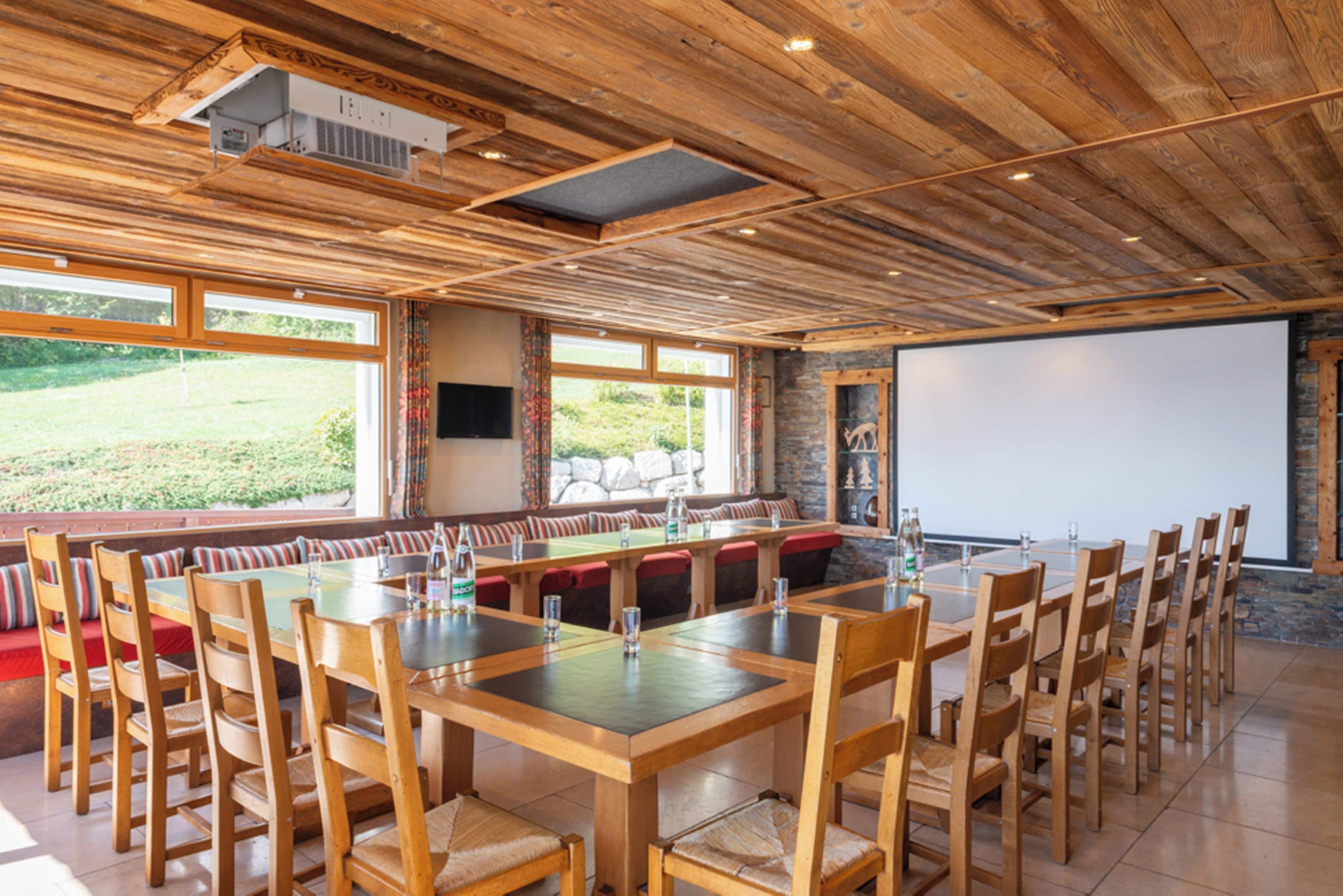 Un comedor amplio con mesas y sillas de madera, ventanas grandes y una pared de piedra.